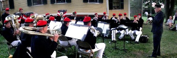A brass band performing on the grass in front of a yellow house.