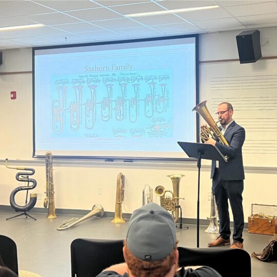 Chris Troiano plays a valved tenor horn while giving a presentation on the Saxhorn valved instrument family.